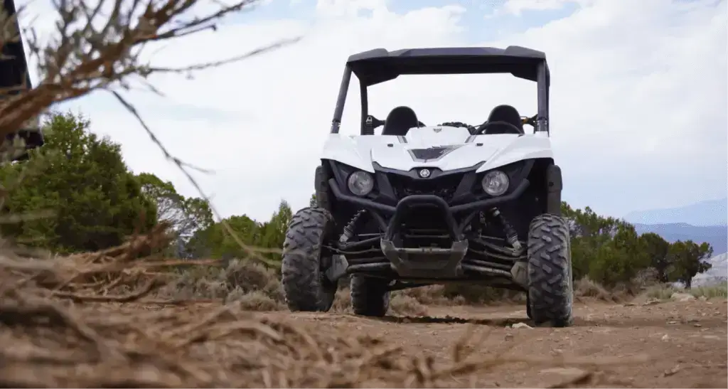 White Yamaha UTV parked on a rugged desert trail under a bright sky.