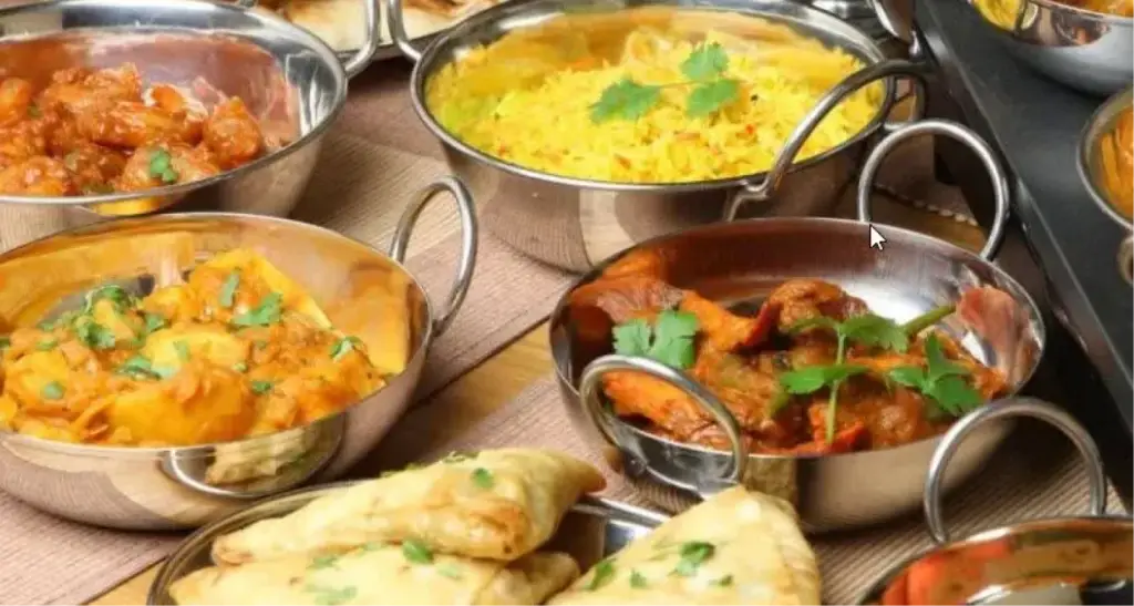 Variety of Indian dishes including curries, rice, and samosas in metal serving bowls.
