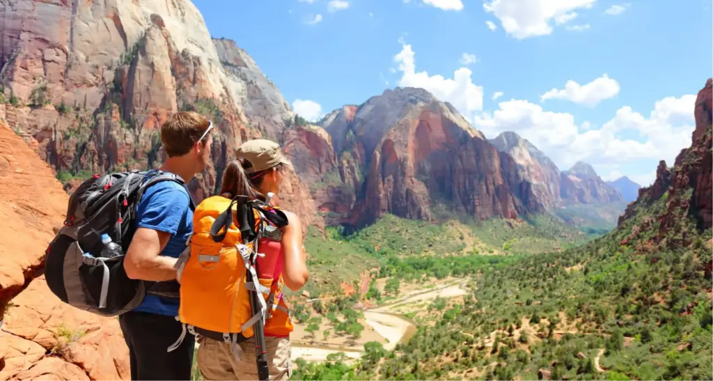 Hikers wearing technical daypacks and outdoor apparel while standing on a cliff edge with a mountain