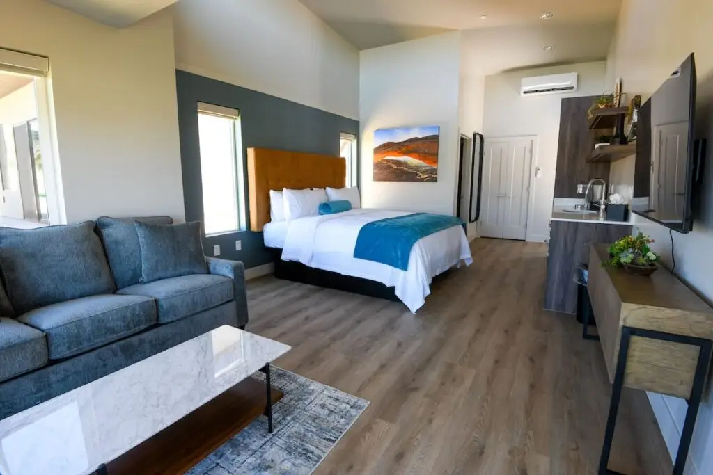 Modern studio villa interior featuring a blue sofa, marble coffee table, and a bed with a mustard headboard and turquoise accents.
