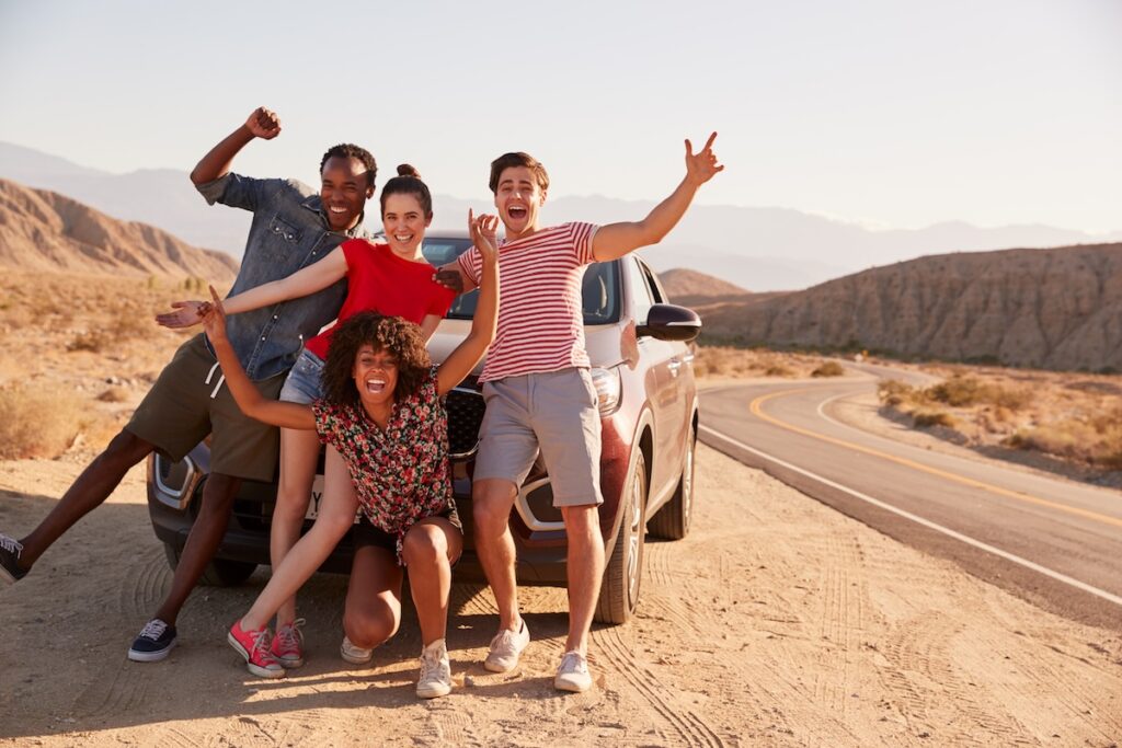 Young adult friends on road trip have fun posing by the car