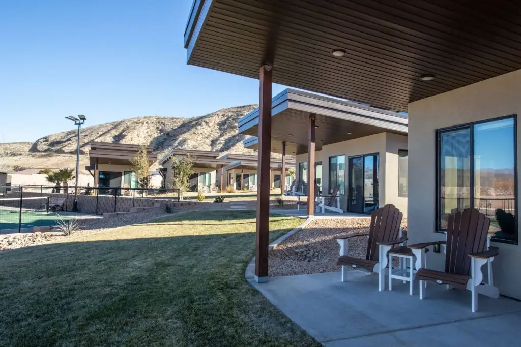 Modern desert resort villas with private patios and Adirondack chairs overlooking a grassy lawn and rugged hills.